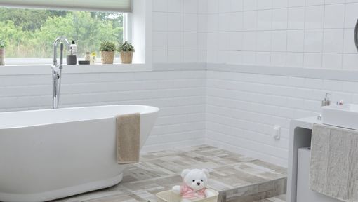 Lyst og moderne baderom med badekar og en bamse som sitter på gulvet