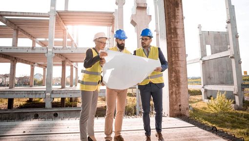 Tre arbeidere ser på en planleggingstegning av en bygningskonstruksjon